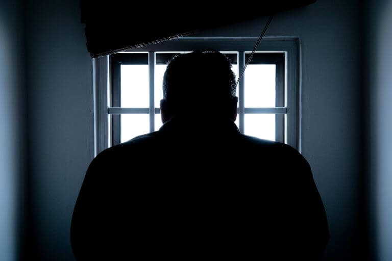 Man staring out  a window with bars